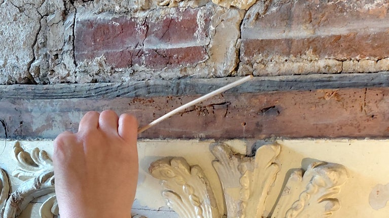 A conservator works on the papier mache detailing of a fireplace